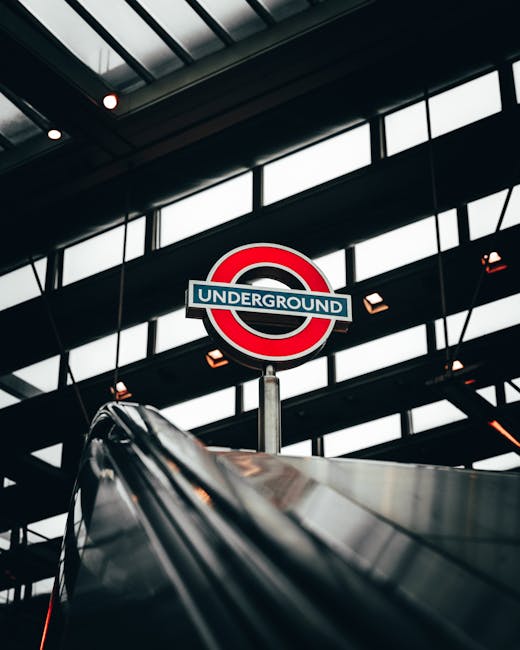 A close-up of a classic London Underground sign mounted on a building facade; the sign features a red circle background with a horizontal blue bar across the middle, displaying the word 'UNDERGROUND'